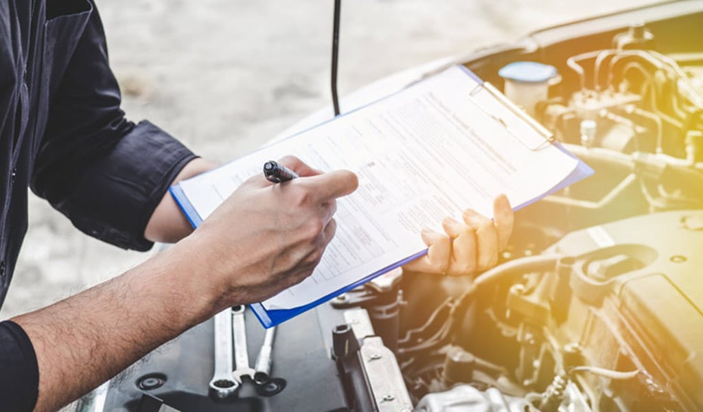 KFZ Meister mit Klemmbrett und Checkliste über geöffneter Motorhaube.