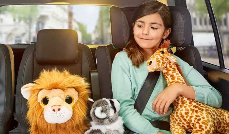 Mädchen sitzt mit Plüschtieren im Auto und lächelt - Autoversicherung ADAC