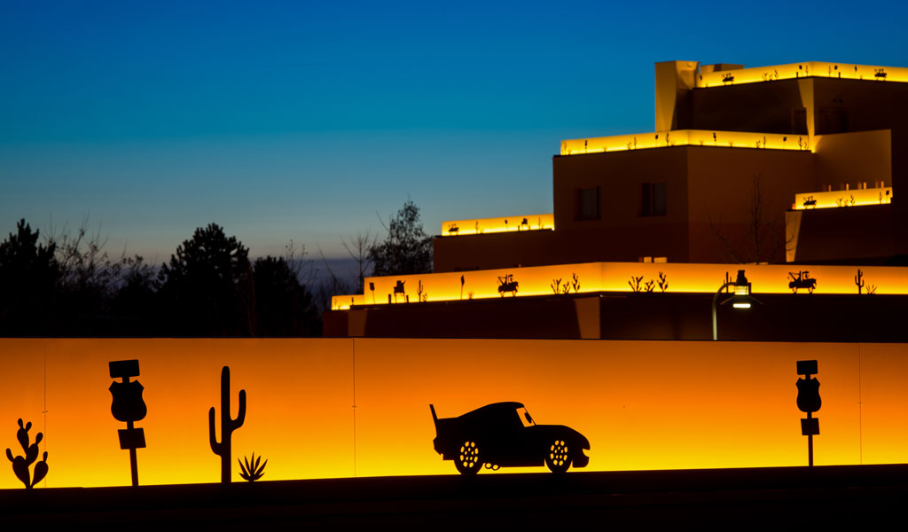 Silhouette von Auto und Kakteen vor einem Gebäude bei Sonnenuntergang mit gelbem Licht.