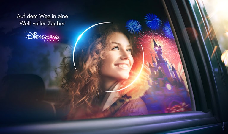 Frau lächelt aus Autofenster; Disneyland Paris im Hintergrund; bunte Feuerwerke; zauberhaftes Ambiente.