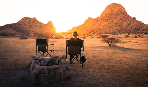 Eine Person sitzt entspannt auf einem Stuhl in einer Wüstenlandschaft bei Sonnenuntergang.