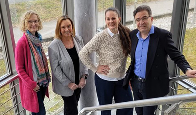 Eine lachende Gruppe von drei Frauen und einem Mann steht auf einer Treppe.