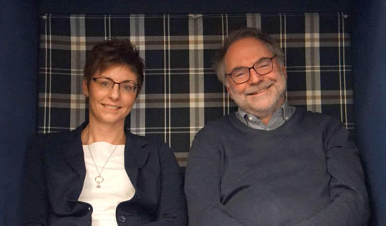 Eine Frau mit braunem Haar und ein Mann mit grauem Haar lächeln freundlich.