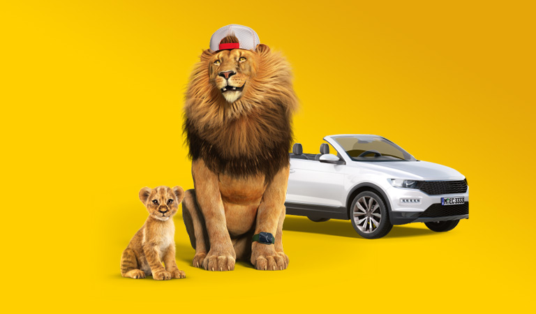 Ein Löwe mit einer Mütze sitzt neben einem Löwenjunges und einem weißen Cabrio.