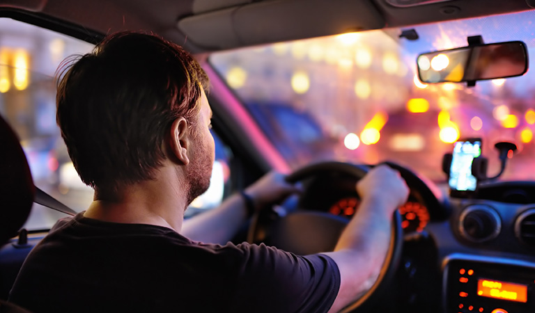 Ein Mann mit konzentriertem Gesichtsausdruck fährt ein Auto bei Nacht.