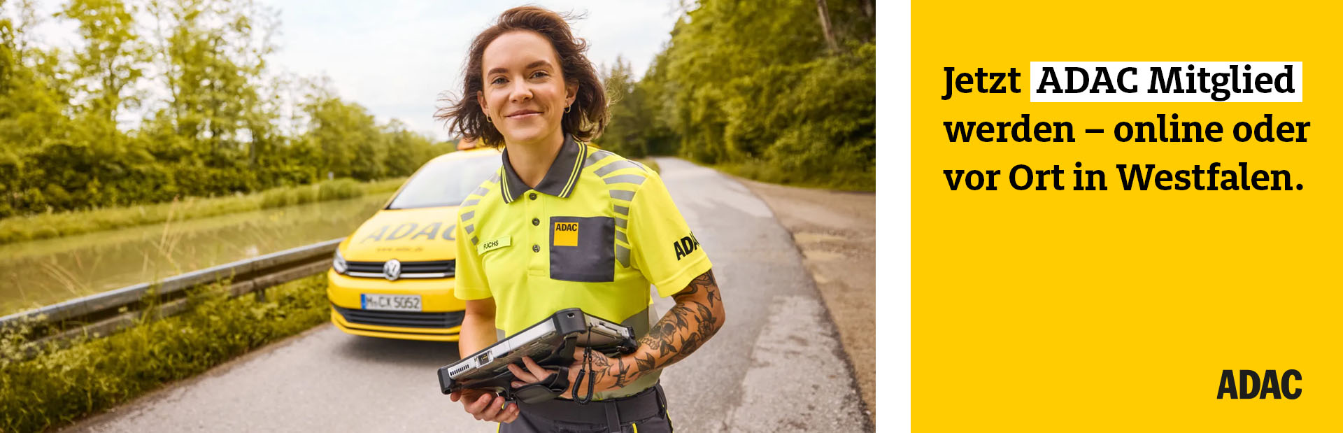 Eine junge Frau mit fröhlichem Gesichtsausdruck steht in gelber ADAC Arbeitskleidung vor einem ADAC Auto auf einer Landstraße und hält ein Diagnosegerät in der Hand