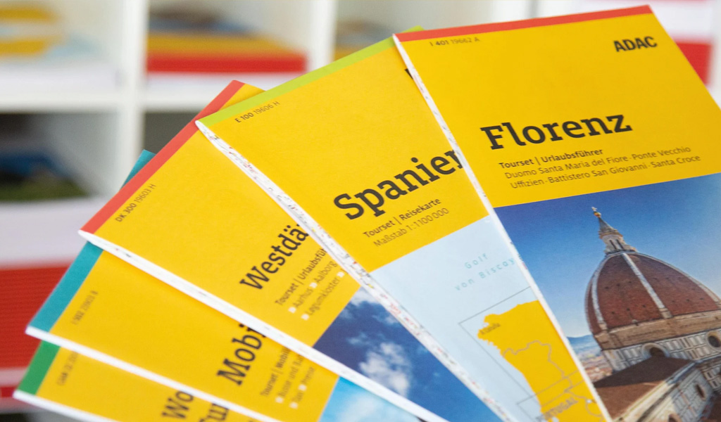 Mehrere bunte Reiseführer mit gelbem Umschlag liegen aufgefächert auf einem Tisch