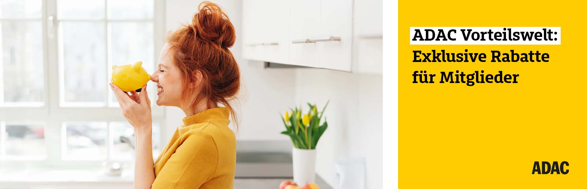 Eine junge Frau mit roten Haaren lächelt und hält ein gelbes Sparschwein in der Küche