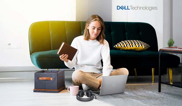 Junge Frau sitzt entspannt mit Laptop und Notizbuch auf hellem Boden vor grünem Sofa