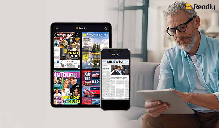 Ein älterer Mann mit grauem Haar und Bart liest entspannt ein Tablet im Wohnzimmer