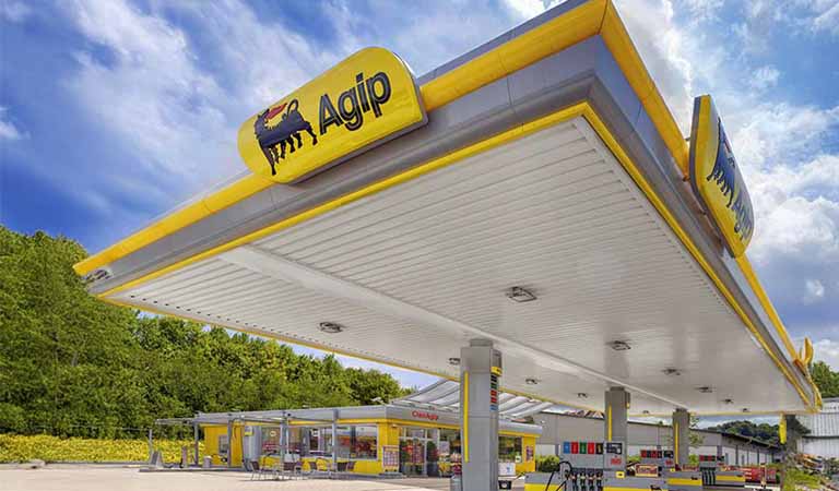Eine Agip Tankstelle mit gelbem und grauem Dach vor grünem Hintergrund und blauem Himmel