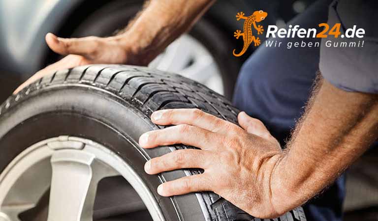 Ein Mann mit neutralem Gesichtsausdruck hält einen schwarzen Autoreifen fest