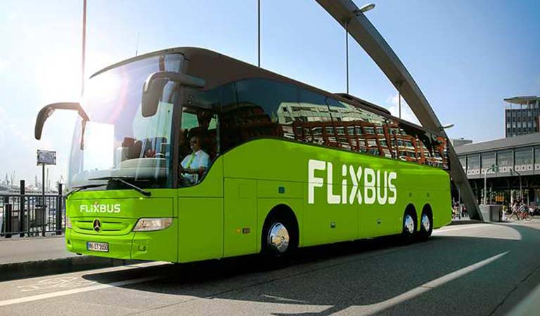 Ein grüner Flixbus mit großem weißen Logo fährt bei Sonnenschein durch die Stadt