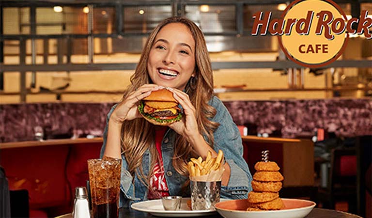 Junge Frau mit langem Haar lächelt und hält einen Burger in einem amerikanischen Restaurant