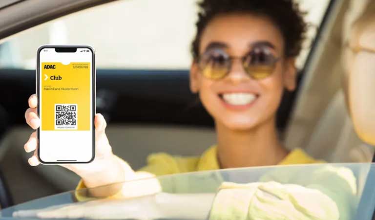 Junge Frau mit hellem Oberteil lächelt und hält eine gelbe ADAC Clubkarte im Auto