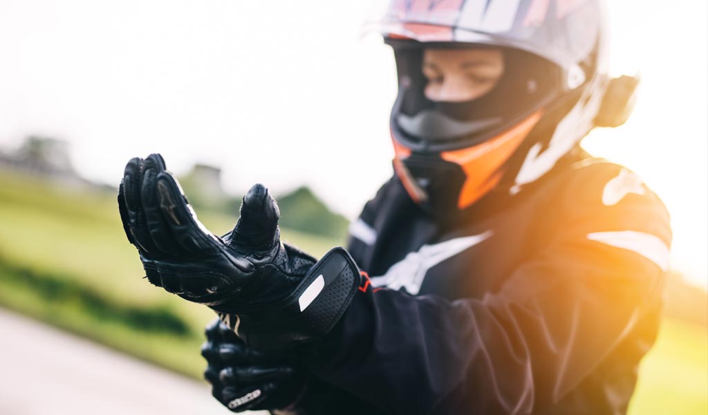 Eine Person mit Motorradhelm zieht schwarze Handschuhe im Freien an
