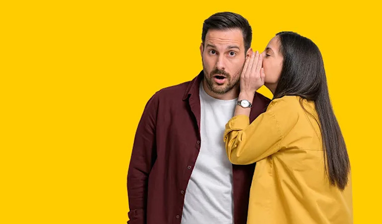 Ein überraschter Mann in bordeauxrotem Hemd hört einer Frau im gelben Hemd zu