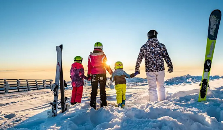 Vier Personen mit bunten Skianzügen stehen fröhlich auf einem verschneiten Hang