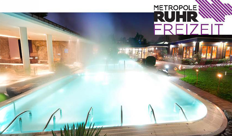 Ein beleuchtetes Außenbecken bei Nacht mit dampfendem Wasser und moderner Umgebung