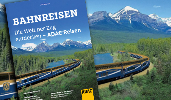 Ein blauer Zug fährt durch grüne Wälder vor schneebedeckten Bergen unter blauem Himmel