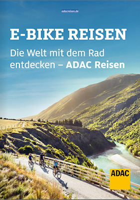 Drei Radfahrer mit Helmen fahren entspannt auf einer Holzbrücke in grüner Berglandschaft