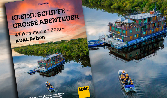 Ein farbenfrohes Flussschiff mit Gästen und einem Beiboot auf einem ruhigen Fluss