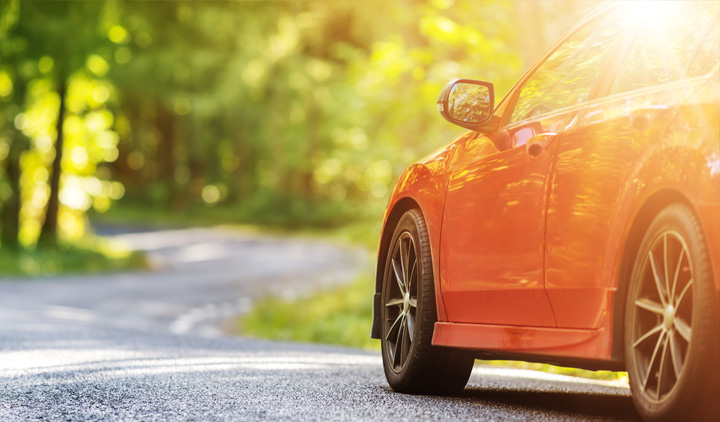 Rotes Auto steht im Sonnenschein am Waldrand auf einer kurvigen Straße