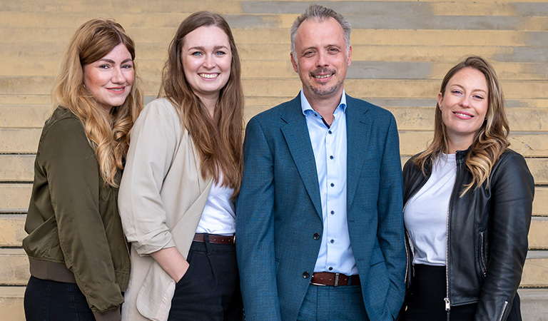 Teamfoto des ADAC Reisebüros Dortmund mit vier lächelnden Mitarbeitenden vor einer Treppe: P. Schulte-Braucks, L. Mertens, M. Krause, A. Tilgner.