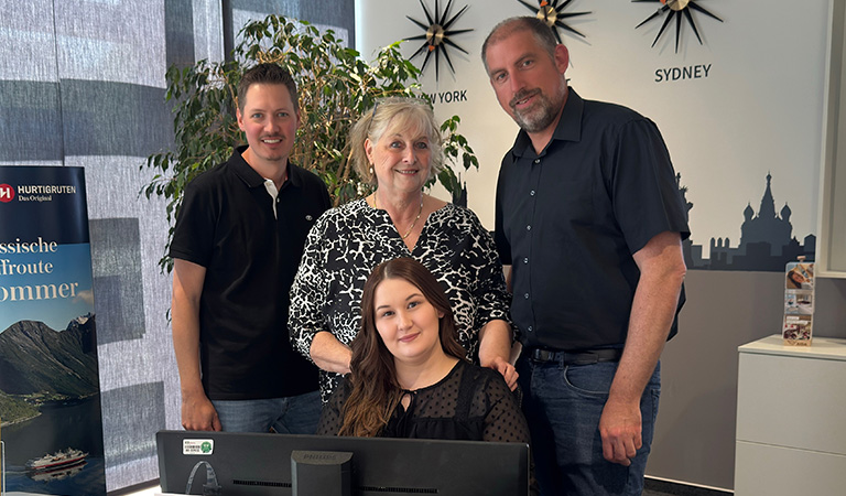 Vier Mitarbeitende des ADAC Reisebüros Soest lächeln in einem Büro mit Weltkarten an der Wand: N. Döring, B. Mauch, M. Beyer und C. Bramkamp.