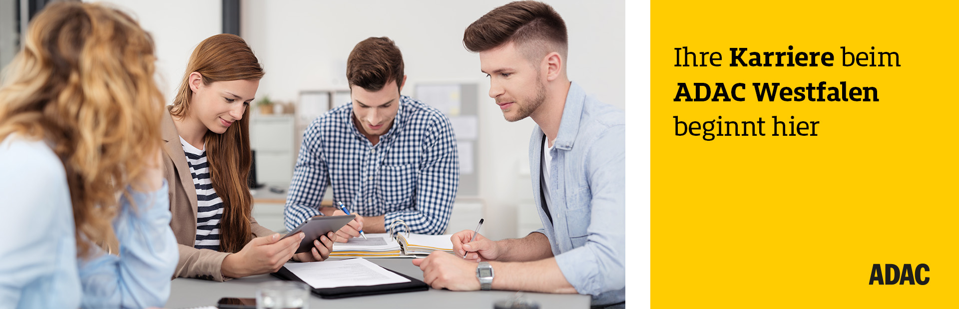 Vier Menschen sitzen am Tisch und schauen konzentriert auf ein Tablet im modernen Büro