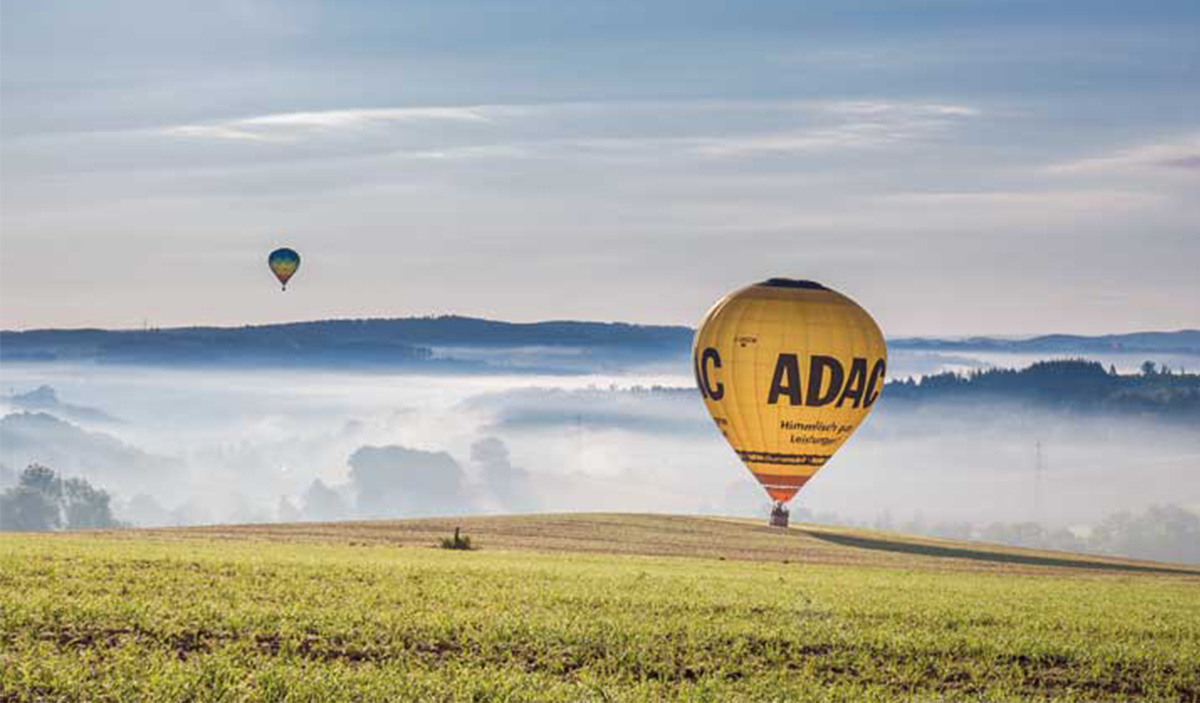 Ein gelber Heißluftballon schwebt über einer grünen Wiese bei Sonnenaufgang