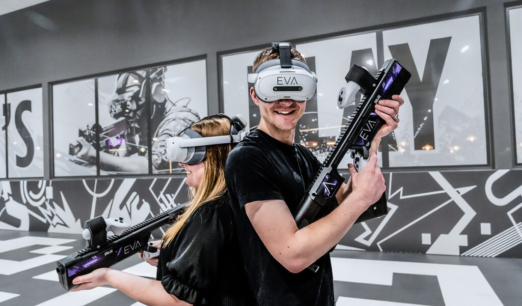 Zwei Personen mit VR Headsets stehen Rücken an Rücken und halten futuristische Controller