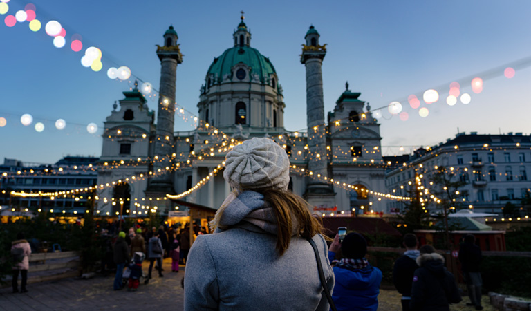 Eine Person mit heller Mütze betrachtet beleuchtete Stände vor einer barocken Kirche
