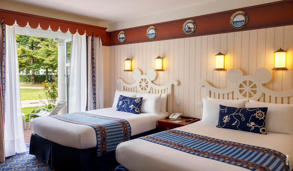 Zwei Einzelbetten mit marineblauer Bettwäsche und Micky-Maus-Kopfleisten im hellen Hotelzimmer