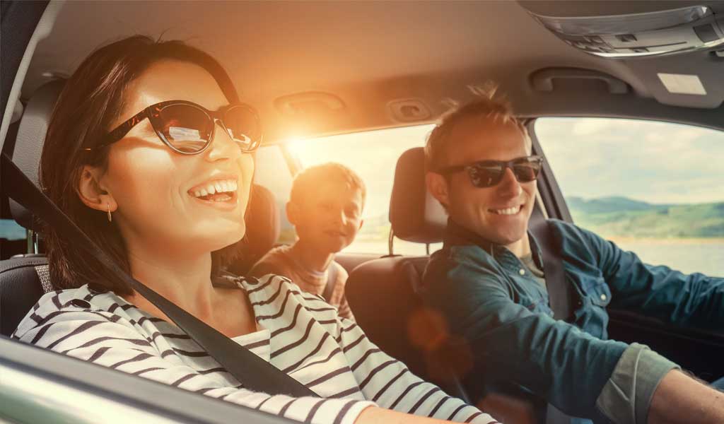 Gut gelaunte Familie mit Kind sitzt im Auto und ist auf dem Weg in den Urlaub.